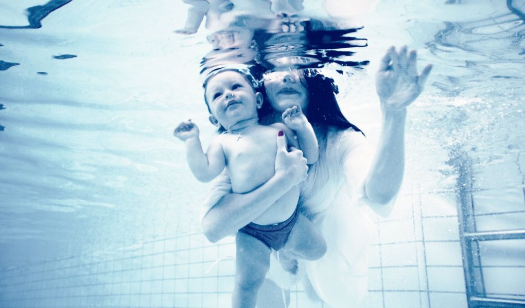 A mom can be seen holding her baby while swimming underwater.