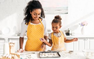 A mother and daughter wear matching aprons while baking cookies.