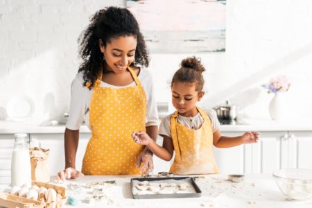 A mother and daughter wear matching aprons while baking cookies.
