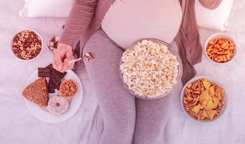 A pregnant woman is surrounded by different bowls of snack food.