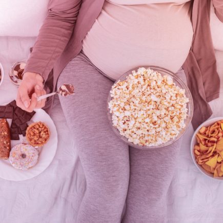 A pregnant woman is surrounded by different bowls of snack food.