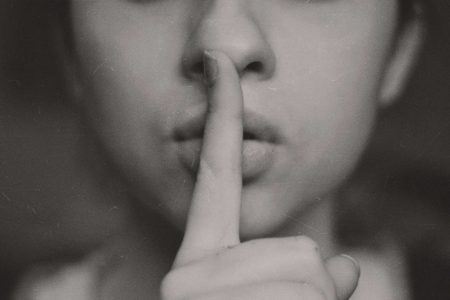 A woman holds a finger to her lips in a shushing gesture.