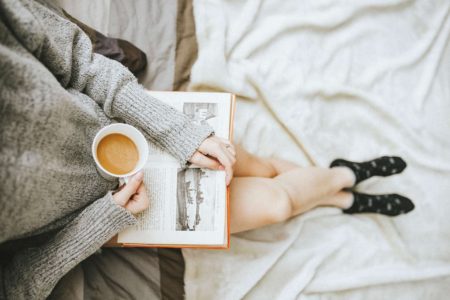 A woman is reading a book and holing a cup of coffee.