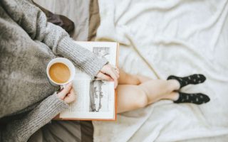 A woman is reading a book and holing a cup of coffee.