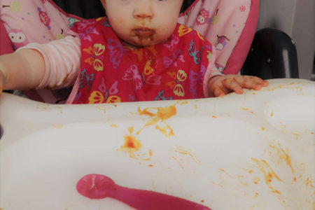 A baby is sitting in a high chair with food all over her face.